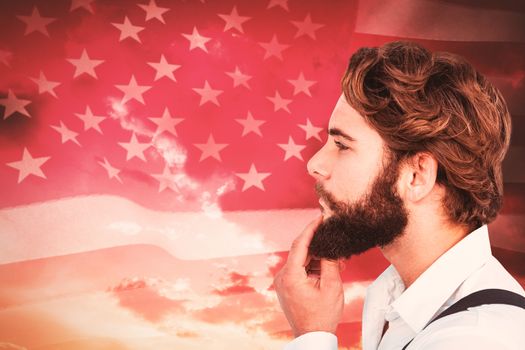 Profile view of hipster touching beard against american flag rippling against sunrise over mountains