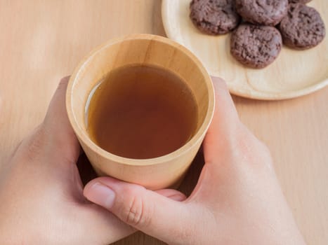 Closeup of female hands holding wood cup of Organic Jasmine Tea with cookies