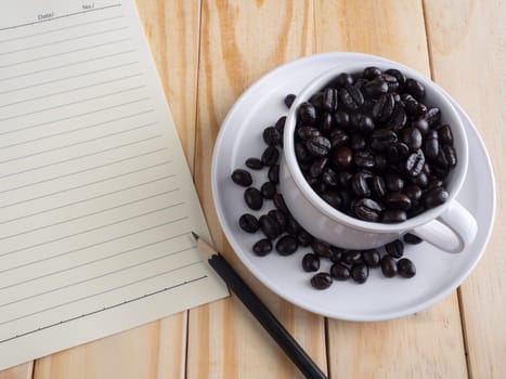 Roasted coffee beans in pretty white cup and memo  on wooden table