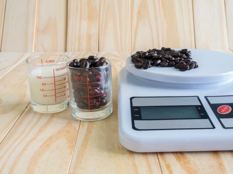 Coffee beans, measuring cup of fresh milk and dIgital balance Scale on wooden board