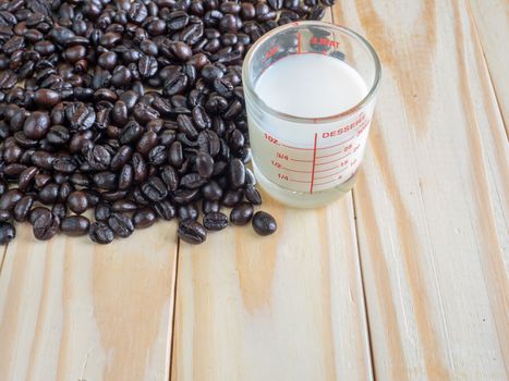 Coffee beans  and a measuring cup of fresh milk on wooden board