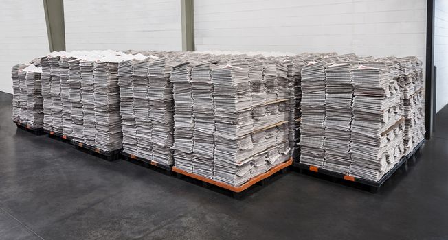 Horizontal shot of multiple stacks of freshly printed newspapers
