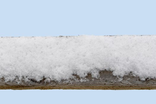 Snow covered old wood fence railing with a light blue sky background