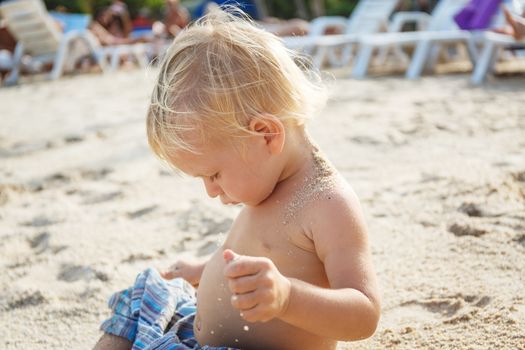 Baby with blond hair on the white sand beach