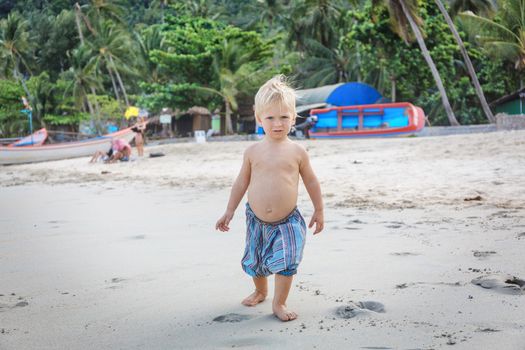 Little boy walking barefoot on white sand beach