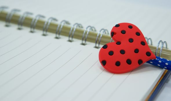 Red heart shape of pencil was placed on reminder book in valentine day.