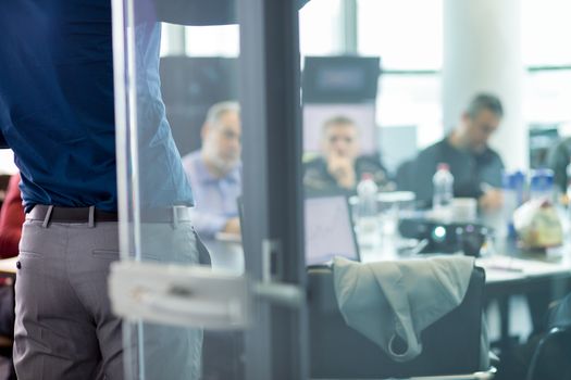 Business man making a presentation at office. Business executive delivering a presentation to his colleagues during meeting or in-house business training. View through glass.