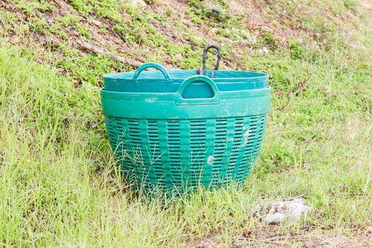 Green plastic trash basket in garden.