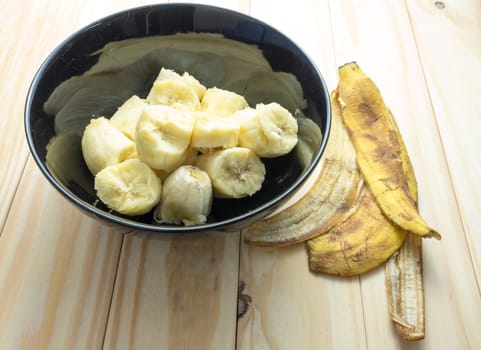 organic banana in black bowl with peels on wooden background