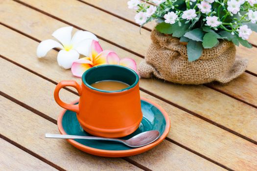 Hot coffee and Plumeria and flowers on the wooden table.Focus on the cup.