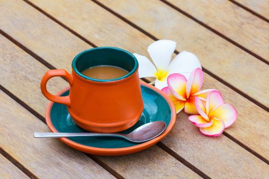 Hot coffee in clay cup and Plumeria flower on the wooden table. Focus on a cup.