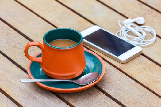 Hot coffee and smart phone and headphone on the wooden table. Focus on a cup.