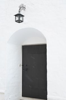 White Abbey wall with lantern and black door in arch