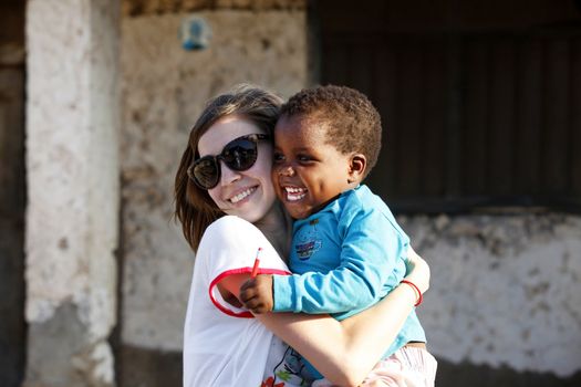 Zanzibar, Tanzania - January 8, 2016: Young woman - a tourist from Russia holds little African girl in her arms in Jambiani. Zanzibar