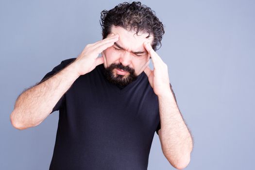 Single overworked man wearing beard rubbing his forehead in pain as if suffering from headache or stress over gray background