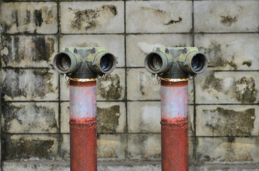 Two red fire hydrant near a cement wall