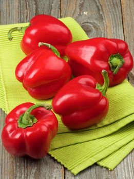 Arrangement of Five Ripe Red Bell Peppers on Green Napkin closeup on Rustic Wooden background