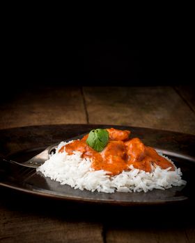 Indian butter chicken on rice photographed on a low Key background.