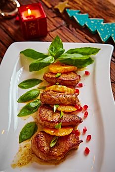 Grilled pork with mandarin oranges decorated with basil on a white plate