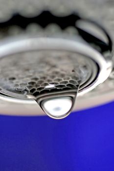 A macro of a white tap / faucet dripping with blue background.