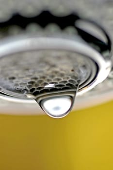 A macro of a white tap / faucet dripping with yellow background.