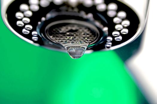 A macro of a white tap / faucet dripping with green background.