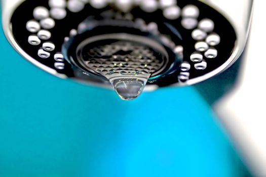 A macro of a white tap / faucet dripping with blue background.