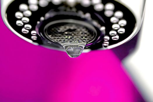 A macro of a white tap / faucet dripping with pink background.