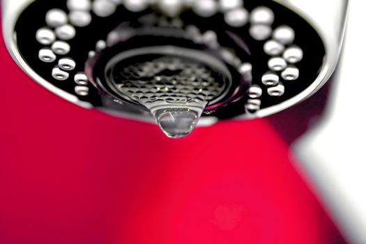 A macro of a white tap / faucet dripping with red background.