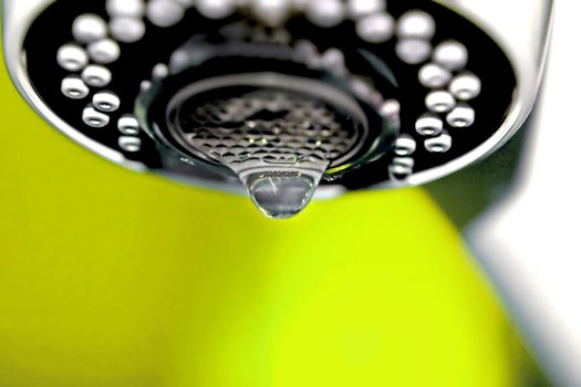 A macro of a white tap / faucet dripping with yellow background.