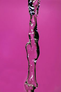 Water falling down, frozen in time with pink background.