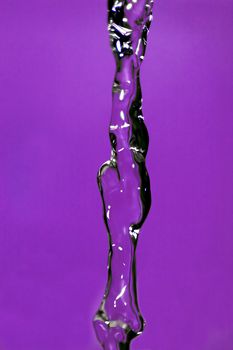 Water falling down, frozen in time with purple background.