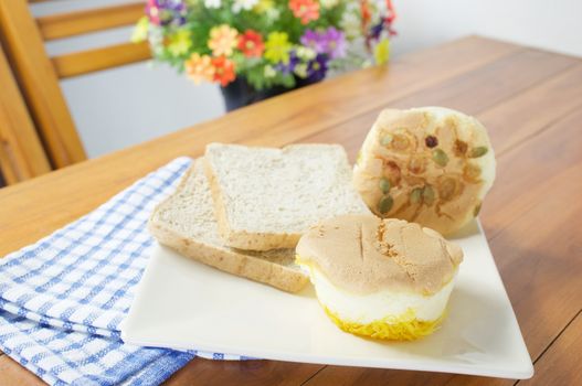 Cup cake with golden threads place in plate with bread on wood table with blue fabric.