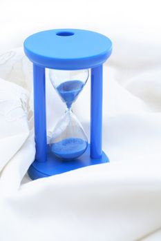 Hourglass with blue sand on nice white textile background