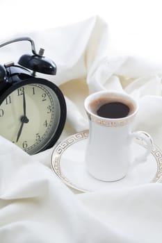 Awakening concept. Alarm clock near cup of coffee on white sheet in bed