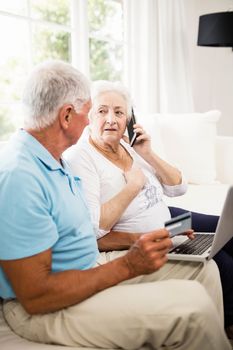 Smiling senior couple using laptop and smartphone at home