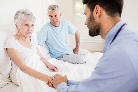 Handsome nurse holding hand of mature woman at home