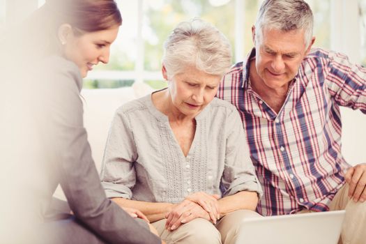 Smiling businesswoman showing laptop monitor to senior couple at home