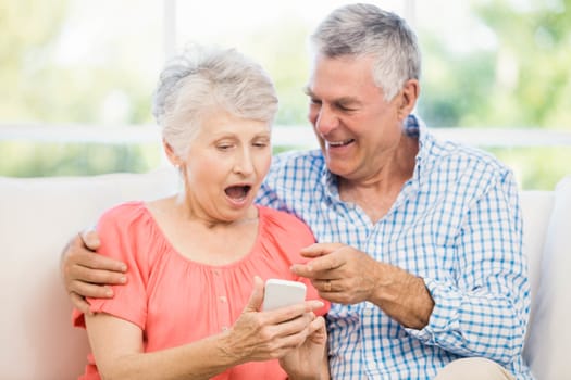 Smiling senior couple using smartphone on the sofa