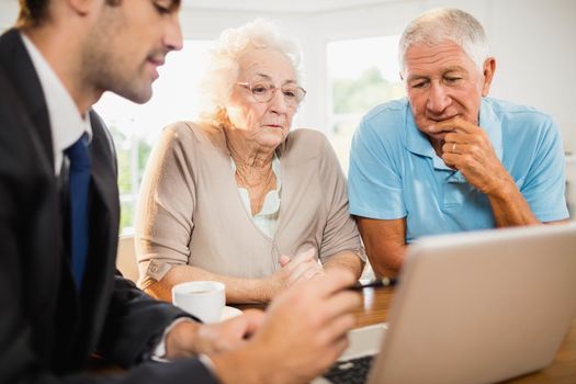 Businessman showing laptop to senior couple at home