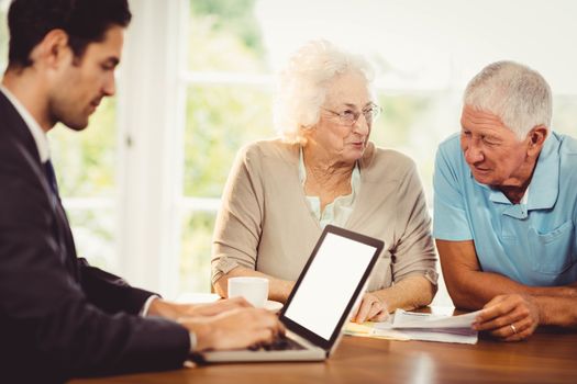 Businessman using laptop while senior couple is reading documents at home