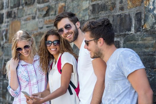 Hip friends looking at smartphone leaning against wall