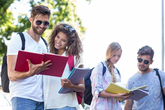 Hip friends reading notes on notebooks outdoors