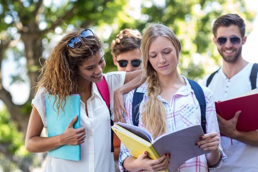 Hip friends reading notes on notebooks outdoors