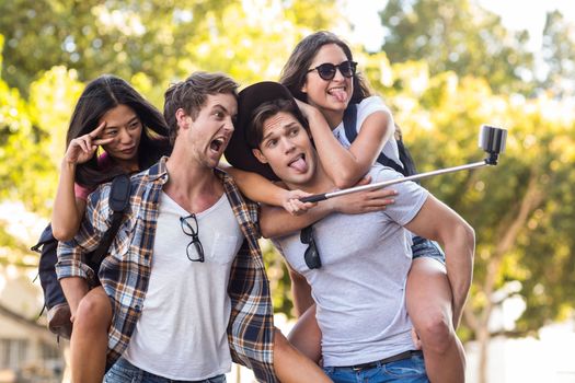 Hip men giving piggy back to their girlfriends and taking selfie on the street