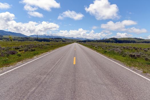 Straight and empty road running through fields. Wyoming.