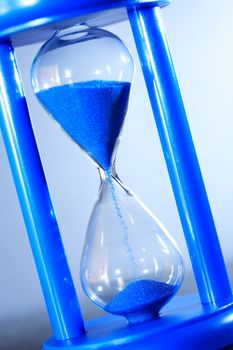 Time concept. Hourglass with blue sand on nice gray background
