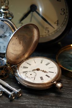 Hour workshop. Vintage still life with ancient silver pocket watch and other clocks