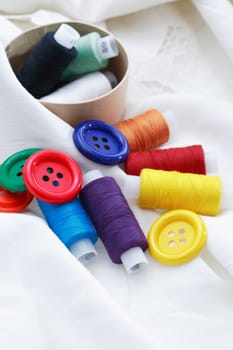 Set of colored thread and buttons on white textile