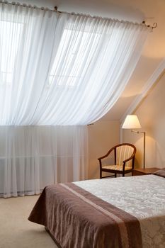 Bedroom in hotel with a big window with curtains, a chair, a bed and a lamp